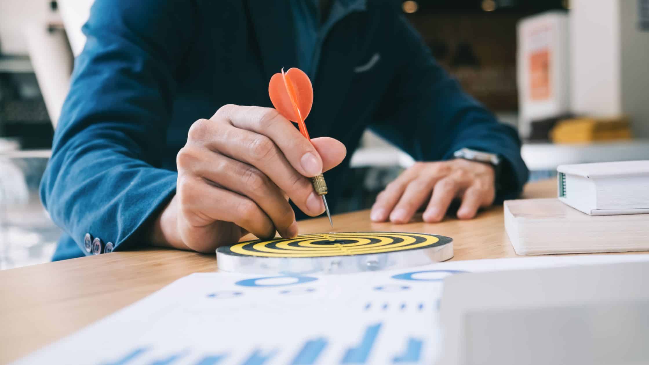 Business man with dart targeting board on desk with stats